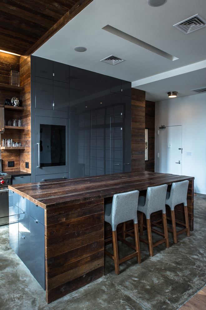 Photo of a mid-sized industrial l-shaped eat-in kitchen in New York with flat-panel cabinets, grey cabinets, wood benchtops, brown splashback, timber splashback, stainless steel appliances, concrete floors, with island and grey floor.