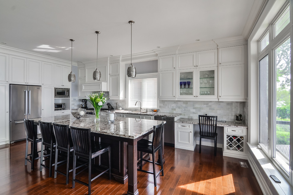 Inspiration for a large traditional l-shaped open plan kitchen in Toronto with an undermount sink, recessed-panel cabinets, white cabinets, granite benchtops, white splashback, subway tile splashback, stainless steel appliances, medium hardwood floors and with island.