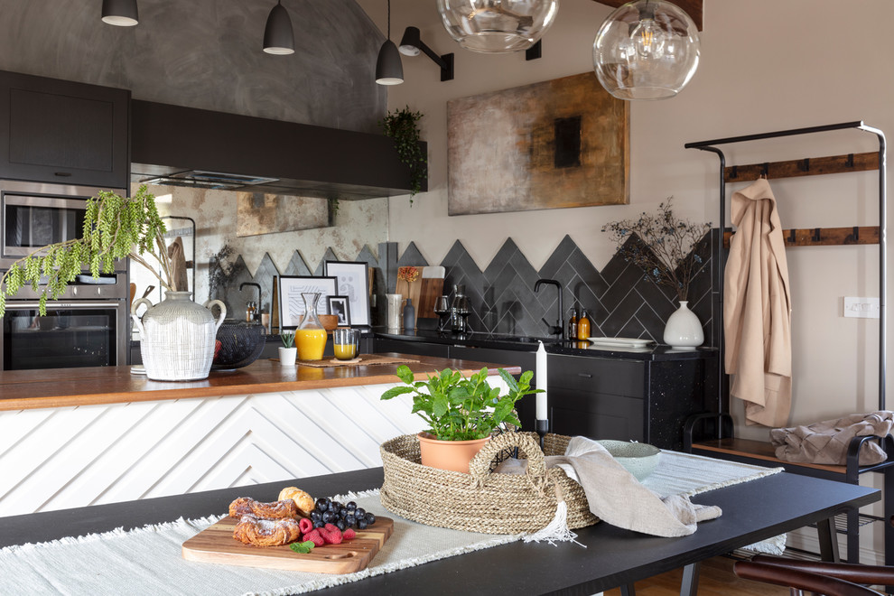 Inspiration for a country l-shaped open plan kitchen in Other with a single-bowl sink, black cabinets, wood benchtops, black splashback, panelled appliances, light hardwood floors, with island, brown floor and brown benchtop.