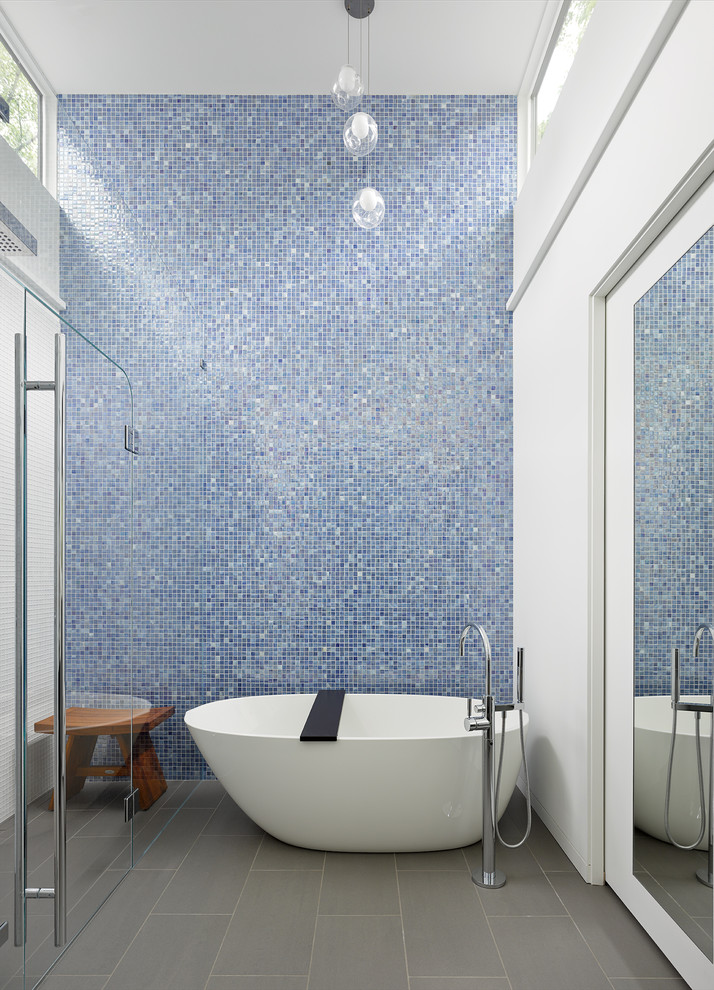 Photo of a mid-sized transitional bathroom in Other with a freestanding tub, an open shower, blue tile, glass tile, white walls, porcelain floors and a hinged shower door.