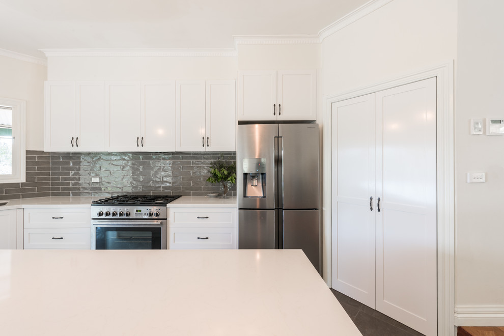 This is an example of a mid-sized country l-shaped kitchen pantry in Melbourne with a double-bowl sink, shaker cabinets, white cabinets, quartz benchtops, green splashback, subway tile splashback, stainless steel appliances, porcelain floors and with island.