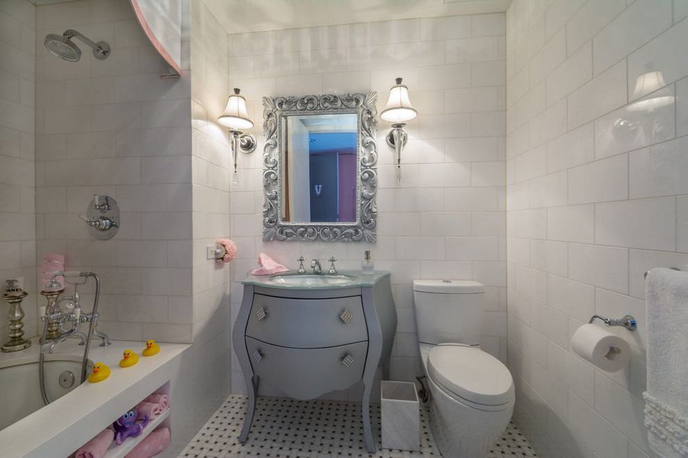 Inspiration for a mid-sized traditional kids bathroom in New York with white walls, ceramic floors, furniture-like cabinets, grey cabinets, an alcove tub, a shower/bathtub combo, a two-piece toilet, white tile, subway tile, an undermount sink, glass benchtops, multi-coloured floor and a shower curtain.