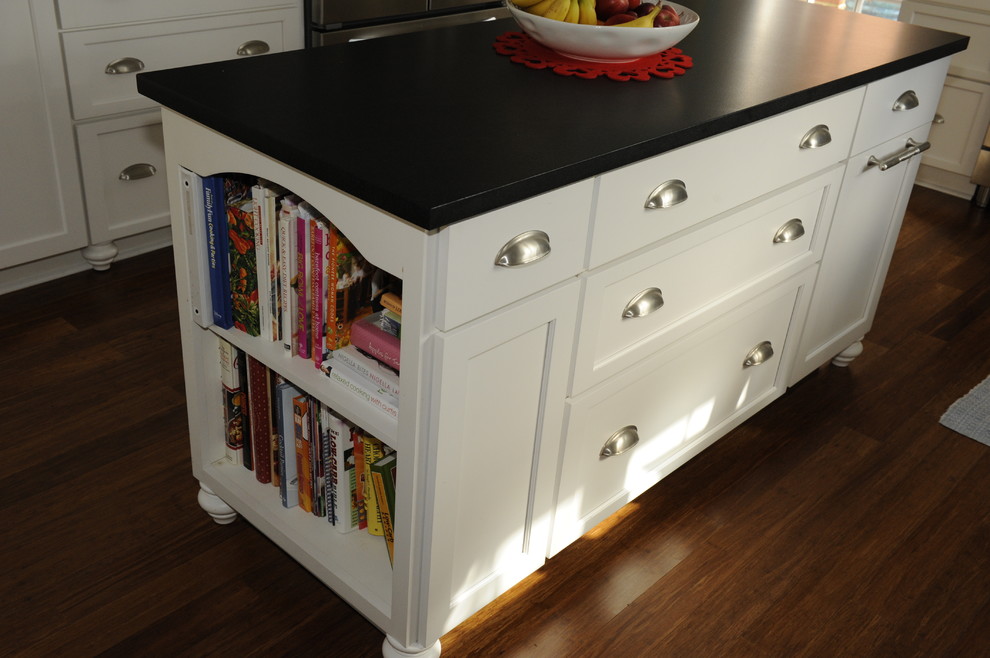 Large transitional u-shaped medium tone wood floor enclosed kitchen photo in Baltimore with a farmhouse sink, glass-front cabinets, white cabinets, soapstone countertops, white backsplash, subway tile backsplash, stainless steel appliances and an island