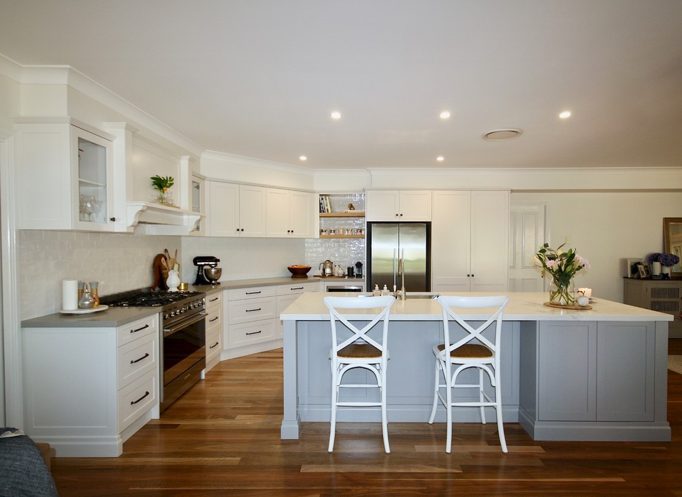 Photo of a large transitional u-shaped eat-in kitchen in Sydney with an undermount sink, shaker cabinets, grey cabinets, quartz benchtops, white splashback, porcelain splashback, stainless steel appliances, medium hardwood floors, with island, brown floor and white benchtop.