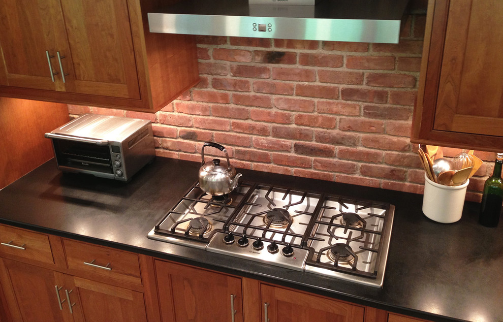 Example of a mid-sized transitional galley gray floor and porcelain tile eat-in kitchen design in New York with an undermount sink, shaker cabinets, medium tone wood cabinets, granite countertops, red backsplash, brick backsplash, stainless steel appliances, no island and black countertops