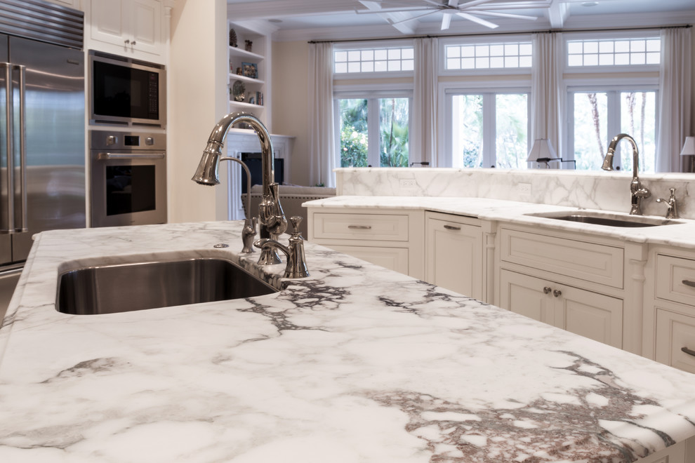 Example of a large transitional u-shaped limestone floor and white floor open concept kitchen design in Orlando with an undermount sink, raised-panel cabinets, white cabinets, marble countertops, gray backsplash, marble backsplash, stainless steel appliances and two islands