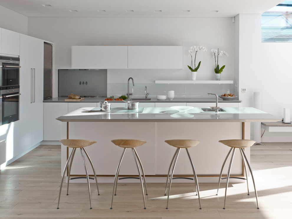 Inspiration for a large contemporary open plan kitchen in London with an undermount sink, flat-panel cabinets, solid surface benchtops, glass sheet splashback, stainless steel appliances and with island.