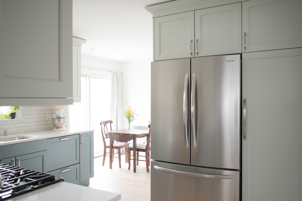 Mid-sized transitional l-shaped light wood floor and beige floor eat-in kitchen photo in Chicago with an undermount sink, shaker cabinets, quartz countertops, white backsplash, mosaic tile backsplash, stainless steel appliances, no island, white countertops and blue cabinets