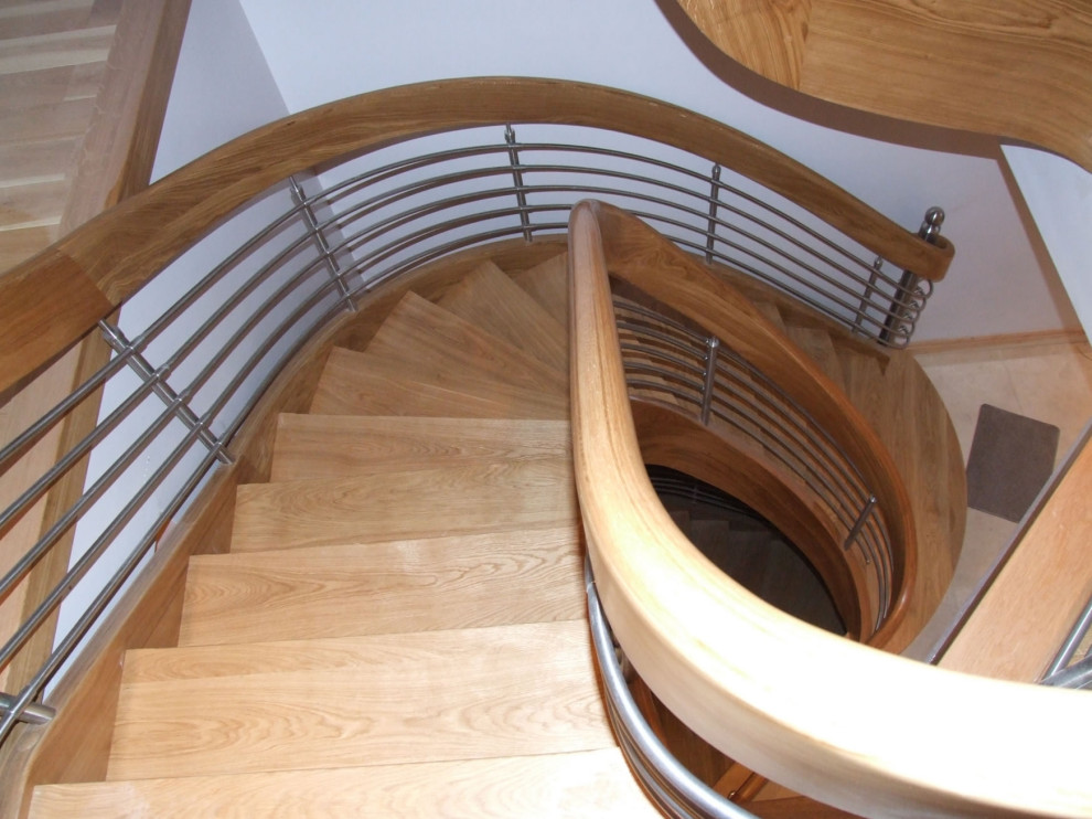 На фото: изогнутая деревянная лестница среднего размера в стиле модернизм с деревянными ступенями и перилами из смешанных материалов с
