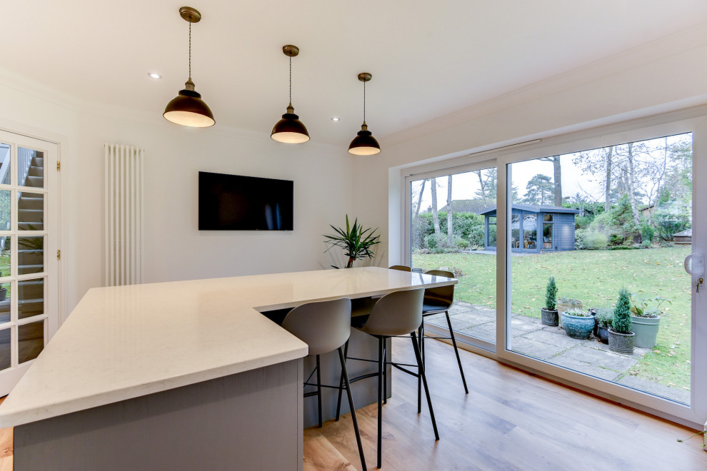 Large contemporary u-shaped open plan kitchen in Sussex with an undermount sink, shaker cabinets, grey cabinets, quartzite benchtops, white splashback, panelled appliances, medium hardwood floors, with island, brown floor and white benchtop.