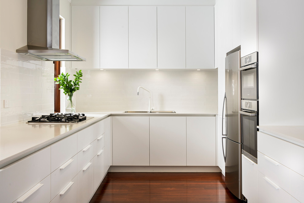 Contemporary u-shaped separate kitchen in Perth with a drop-in sink, flat-panel cabinets, white cabinets, white splashback, subway tile splashback, dark hardwood floors, no island, brown floor and white benchtop.