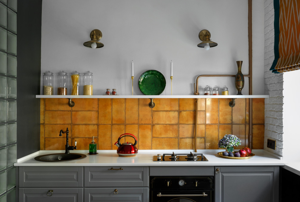 This is an example of a small contemporary single-wall eat-in kitchen in Moscow with an undermount sink, shaker cabinets, grey cabinets, solid surface benchtops, orange splashback, ceramic splashback, black appliances, ceramic floors, no island, multi-coloured floor and white benchtop.
