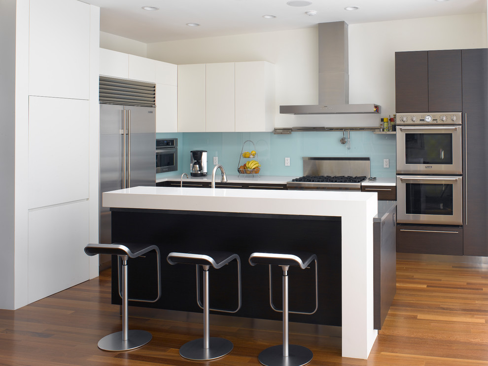 Design ideas for a large modern l-shaped kitchen in San Francisco with flat-panel cabinets, blue splashback, glass sheet splashback, stainless steel appliances, dark hardwood floors, with island, brown floor, an undermount sink, white cabinets and quartz benchtops.