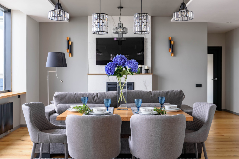 Inspiration pour une salle à manger ouverte sur la cuisine design avec un mur gris, parquet clair, une cheminée standard et un sol beige.