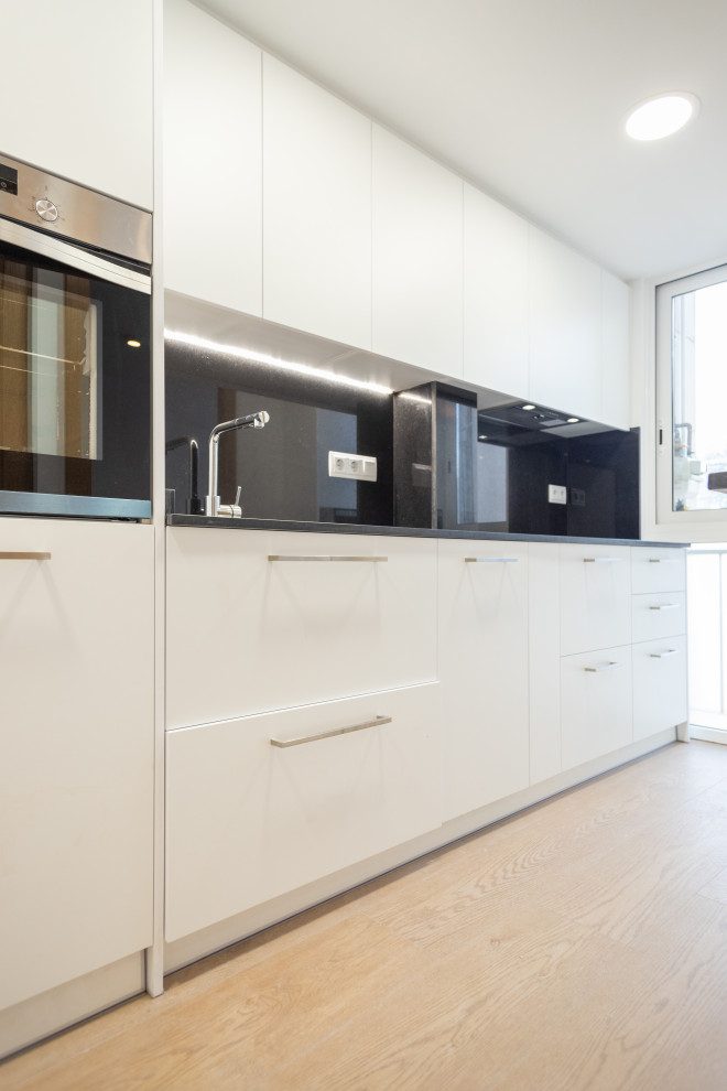 Inspiration for a medium sized contemporary single-wall enclosed kitchen in Barcelona with a single-bowl sink, white cabinets, black splashback, stainless steel appliances, ceramic flooring, no island, brown floors and black worktops.
