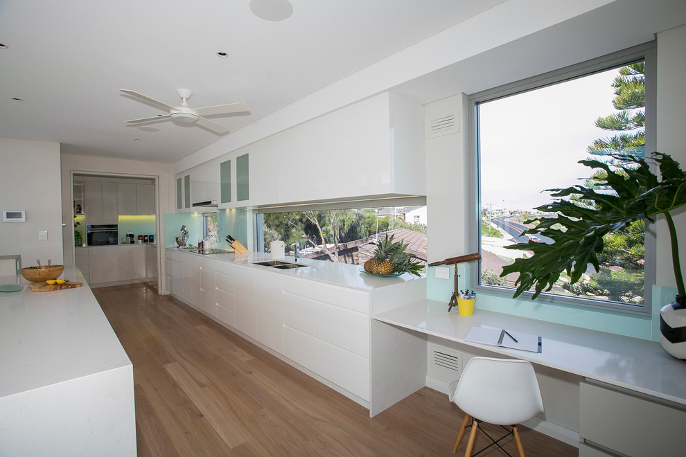 Inspiration for a tropical galley kitchen in Perth with an undermount sink, quartz benchtops, glass sheet splashback, light hardwood floors and with island.