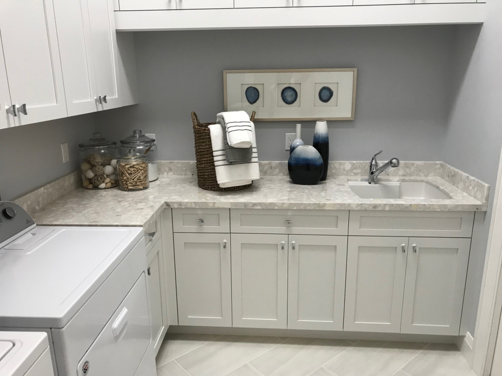 Design ideas for a mid-sized l-shaped dedicated laundry room in Miami with a drop-in sink, recessed-panel cabinets, white cabinets, granite benchtops, grey walls, ceramic floors, a side-by-side washer and dryer, grey floor and multi-coloured benchtop.