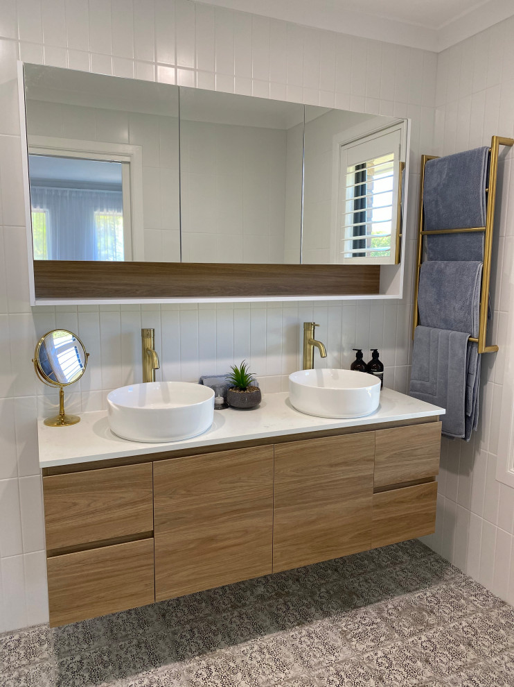 Inspiration for a medium sized modern ensuite bathroom in Melbourne with light wood cabinets, a walk-in shower, a one-piece toilet, white tiles, ceramic tiles, white walls, ceramic flooring, a vessel sink, engineered stone worktops, multi-coloured floors, an open shower, multi-coloured worktops, double sinks and a floating vanity unit.