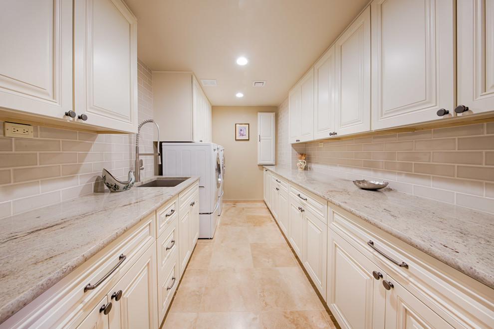 Large traditional galley dedicated laundry room in Phoenix with an undermount sink, raised-panel cabinets, white cabinets, quartzite benchtops, beige walls, travertine floors, a side-by-side washer and dryer and beige floor.