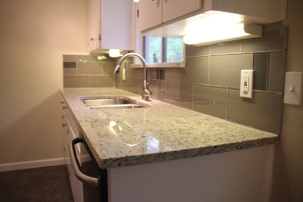 Example of a small transitional u-shaped slate floor enclosed kitchen design in Austin with an undermount sink, white cabinets, granite countertops, glass tile backsplash, stainless steel appliances, flat-panel cabinets, gray backsplash and no island