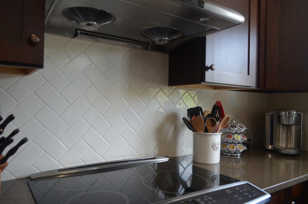 Kitchen pantry - mid-sized transitional l-shaped porcelain tile kitchen pantry idea in New York with shaker cabinets, dark wood cabinets, quartz countertops, white backsplash, subway tile backsplash, stainless steel appliances and an island
