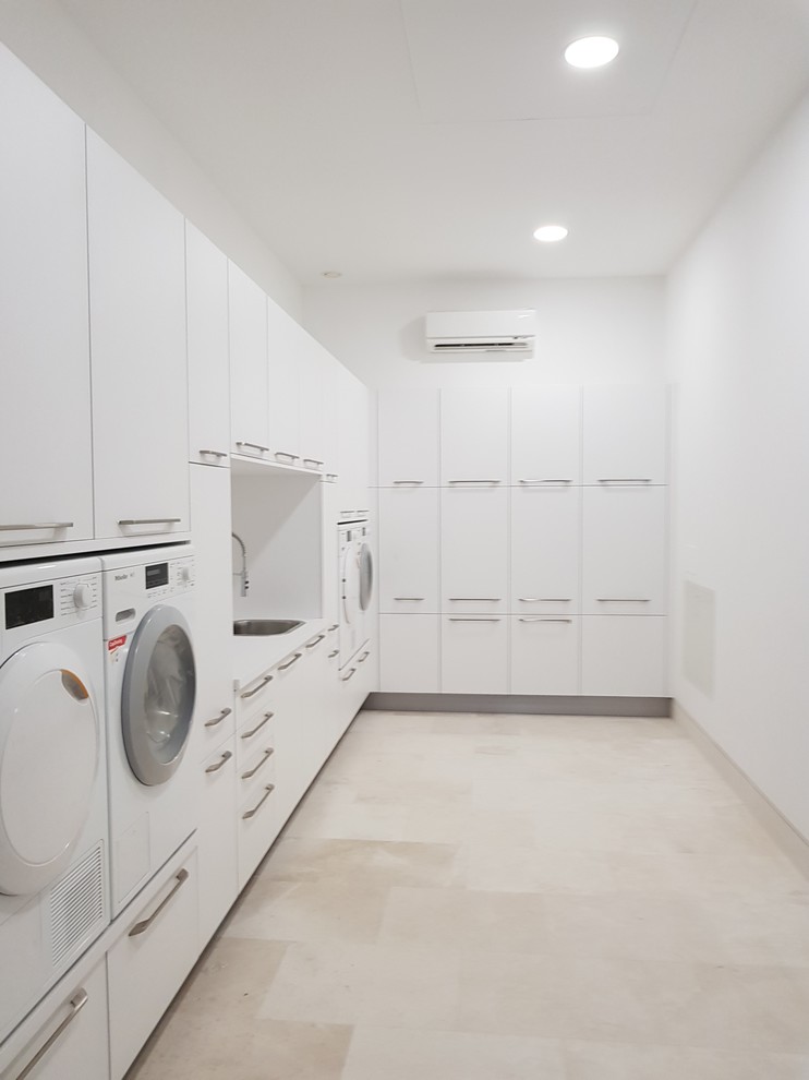 This is an example of a large contemporary l-shaped laundry room in Malaga with flat-panel cabinets, white cabinets, laminate benchtops, white splashback, ceramic splashback, porcelain floors, white walls, beige floor and a drop-in sink.
