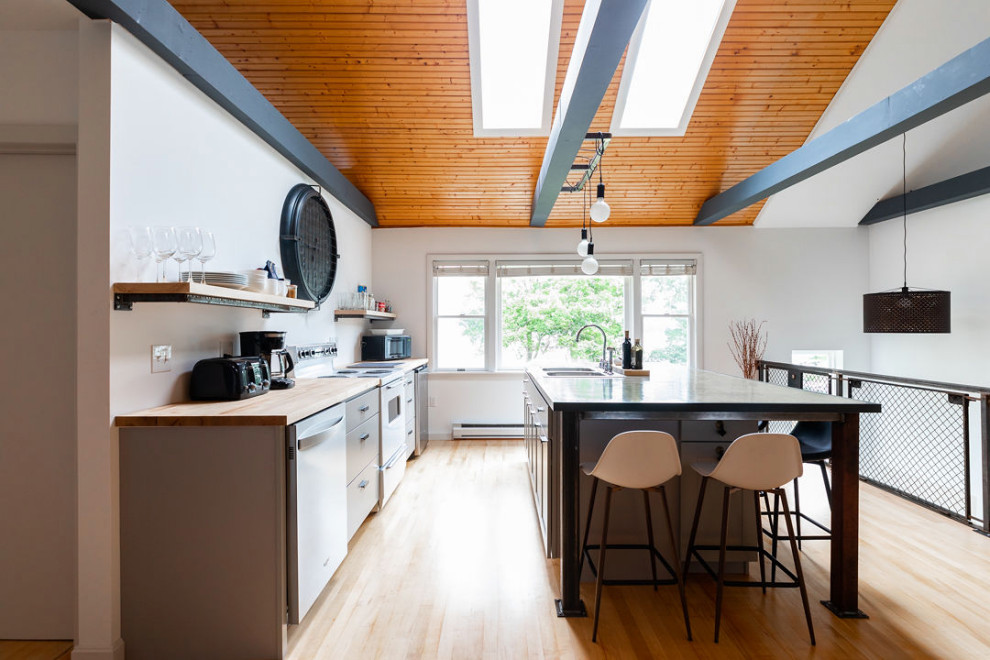 Design ideas for a medium sized industrial single-wall open plan kitchen in Portland Maine with a double-bowl sink, flat-panel cabinets, grey cabinets, concrete worktops, stainless steel appliances, light hardwood flooring, an island, grey worktops and exposed beams.
