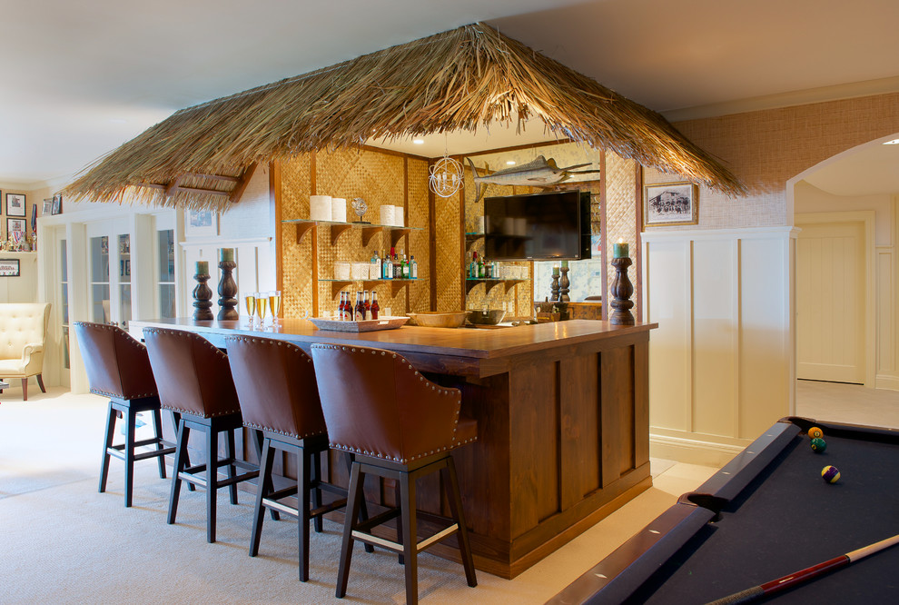 This is an example of a mid-sized tropical seated home bar in New York with dark wood cabinets, wood benchtops, mirror splashback, carpet and brown benchtop.
