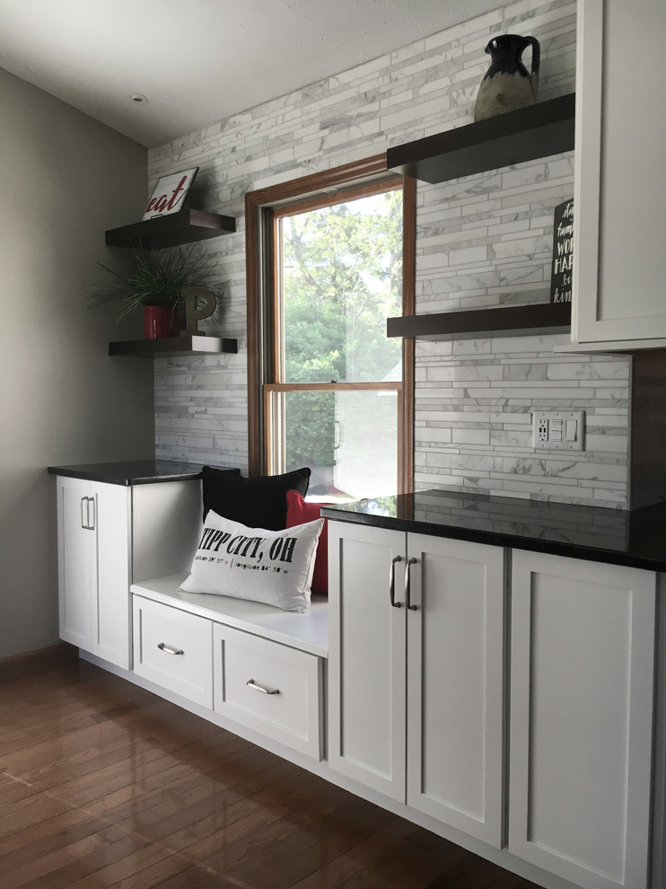Inspiration for a large transitional single-wall medium tone wood floor eat-in kitchen remodel with an undermount sink, shaker cabinets, white cabinets, granite countertops, multicolored backsplash, marble backsplash, stainless steel appliances, an island and black countertops