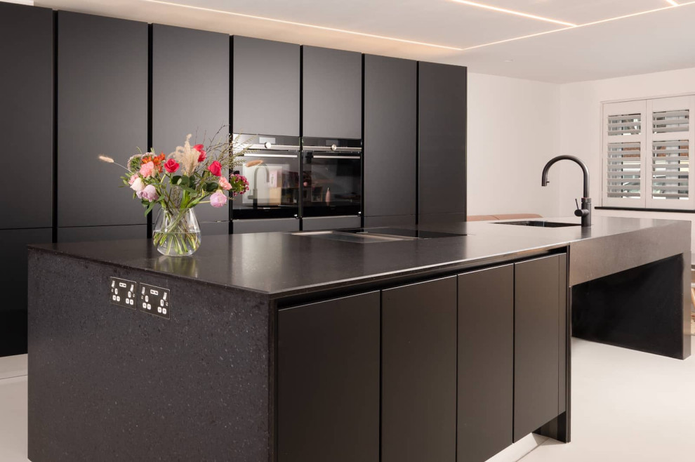Design ideas for a large modern single-wall open plan kitchen in Hertfordshire with flat-panel cabinets, black cabinets, quartzite benchtops, black splashback, black appliances, with island, white floor and black benchtop.