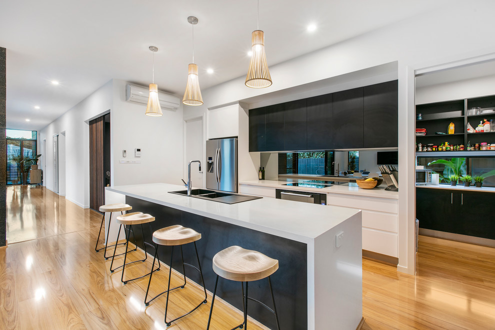 This is an example of a contemporary galley kitchen in Brisbane with a double-bowl sink, flat-panel cabinets, black cabinets, stainless steel appliances, light hardwood floors and with island.