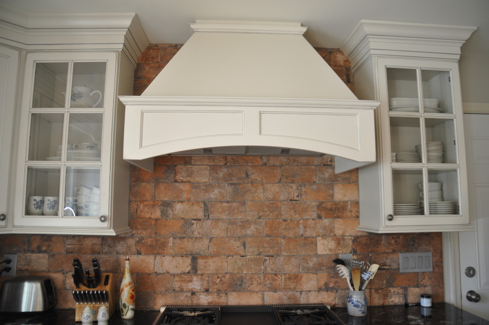 Example of a mid-sized mountain style u-shaped medium tone wood floor eat-in kitchen design in Baltimore with a farmhouse sink, recessed-panel cabinets, white cabinets, granite countertops, red backsplash, stone tile backsplash, stainless steel appliances and an island