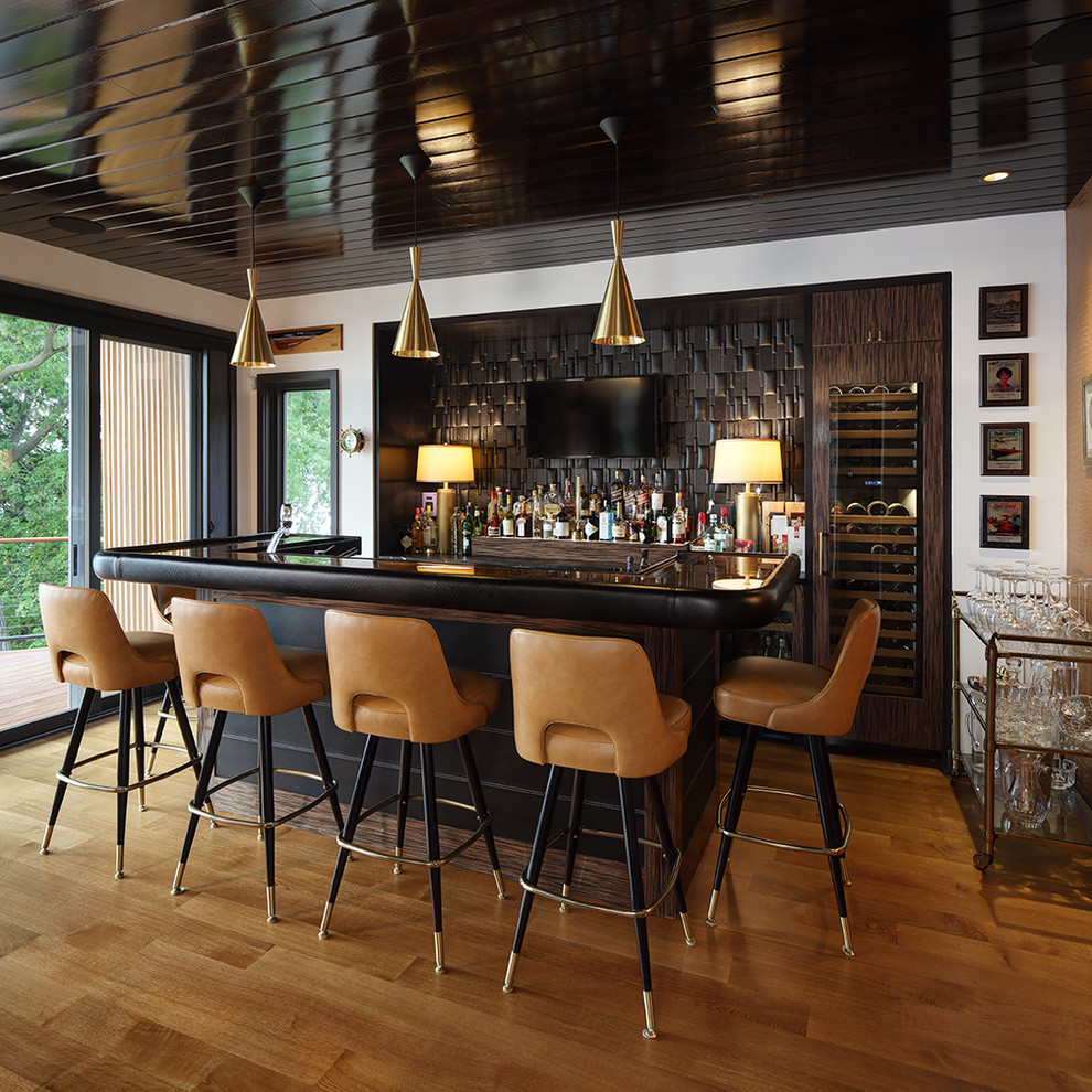 This is an example of a contemporary galley seated home bar in Milwaukee with black splashback and medium hardwood floors.