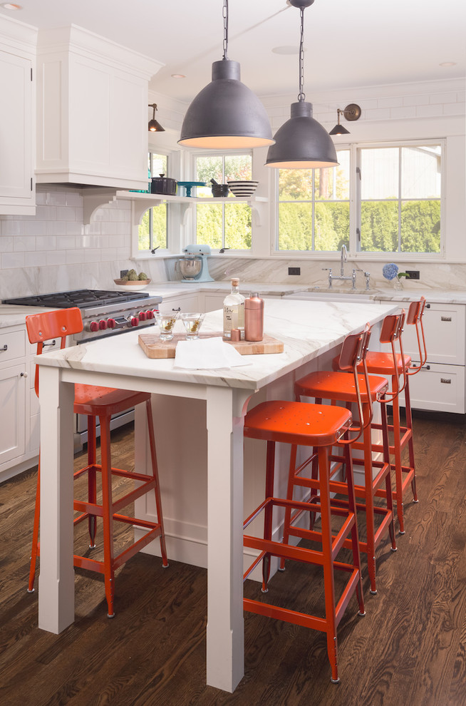 Design ideas for a beach style l-shaped kitchen in Seattle with a farmhouse sink, shaker cabinets, white cabinets, white splashback, stainless steel appliances, dark hardwood floors, with island, brown floor, marble benchtops and subway tile splashback.