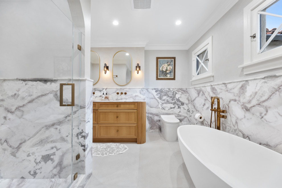 Example of a mid-sized tuscan master marble tile double-sink freestanding bathtub design in Los Angeles with raised-panel cabinets, brown cabinets, an undermount sink, marble countertops, a hinged shower door and a freestanding vanity