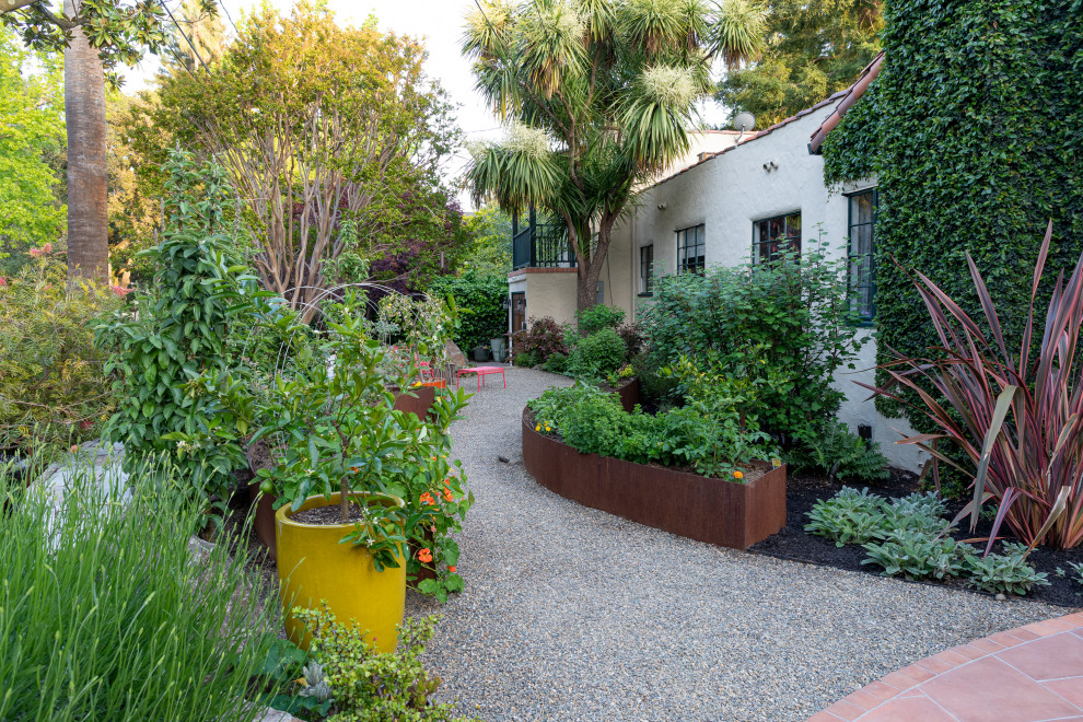 Пример оригинального дизайна: солнечный засухоустойчивый сад среднего размера на переднем дворе в средиземноморском стиле с высокими грядками, хорошей освещенностью, покрытием из гравия и с металлическим забором