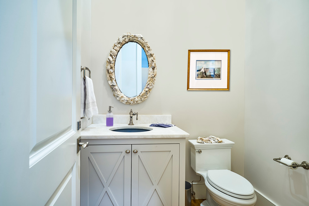 Small transitional powder room in Charleston with grey cabinets, a one-piece toilet, an undermount sink, white tile, beige walls, medium hardwood floors, granite benchtops and white benchtops.