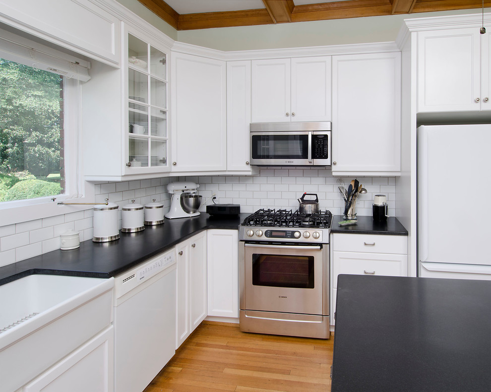 Enclosed kitchen - mid-sized transitional u-shaped medium tone wood floor and brown floor enclosed kitchen idea with a farmhouse sink, shaker cabinets, white cabinets, granite countertops, white backsplash, ceramic backsplash, stainless steel appliances and an island