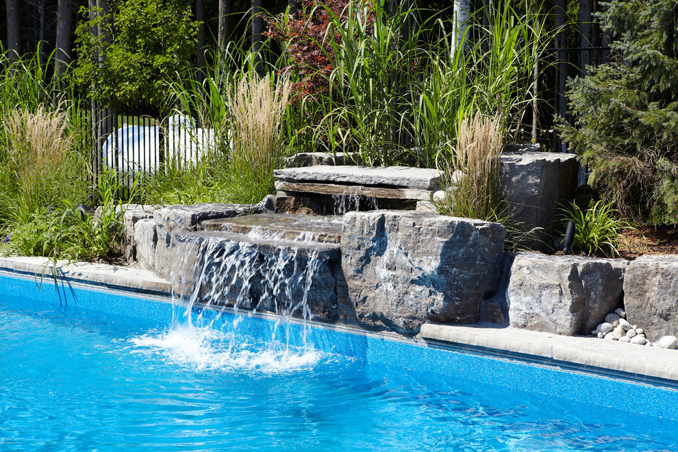 This is an example of a large contemporary backyard rectangular lap pool in Toronto with a water feature and brick pavers.