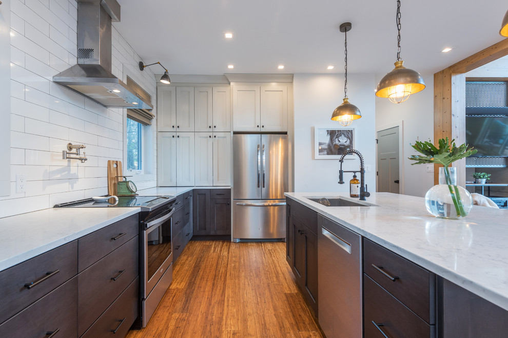 Kitchen - transitional l-shaped medium tone wood floor and brown floor kitchen idea with an undermount sink, shaker cabinets, gray cabinets, white backsplash, stainless steel appliances, an island and white countertops