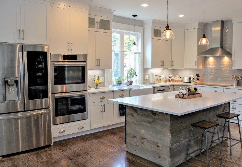 Inspiration for a transitional l-shaped medium tone wood floor and brown floor kitchen pantry remodel with a farmhouse sink, recessed-panel cabinets, white cabinets, quartz countertops, gray backsplash, porcelain backsplash, stainless steel appliances, an island and white countertops