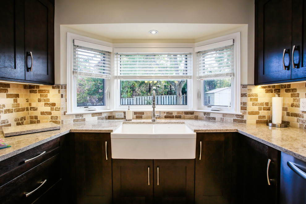 Enclosed kitchen - mid-sized transitional u-shaped porcelain tile enclosed kitchen idea in Toronto with a farmhouse sink, shaker cabinets, dark wood cabinets, quartz countertops, beige backsplash, stone tile backsplash, stainless steel appliances and no island
