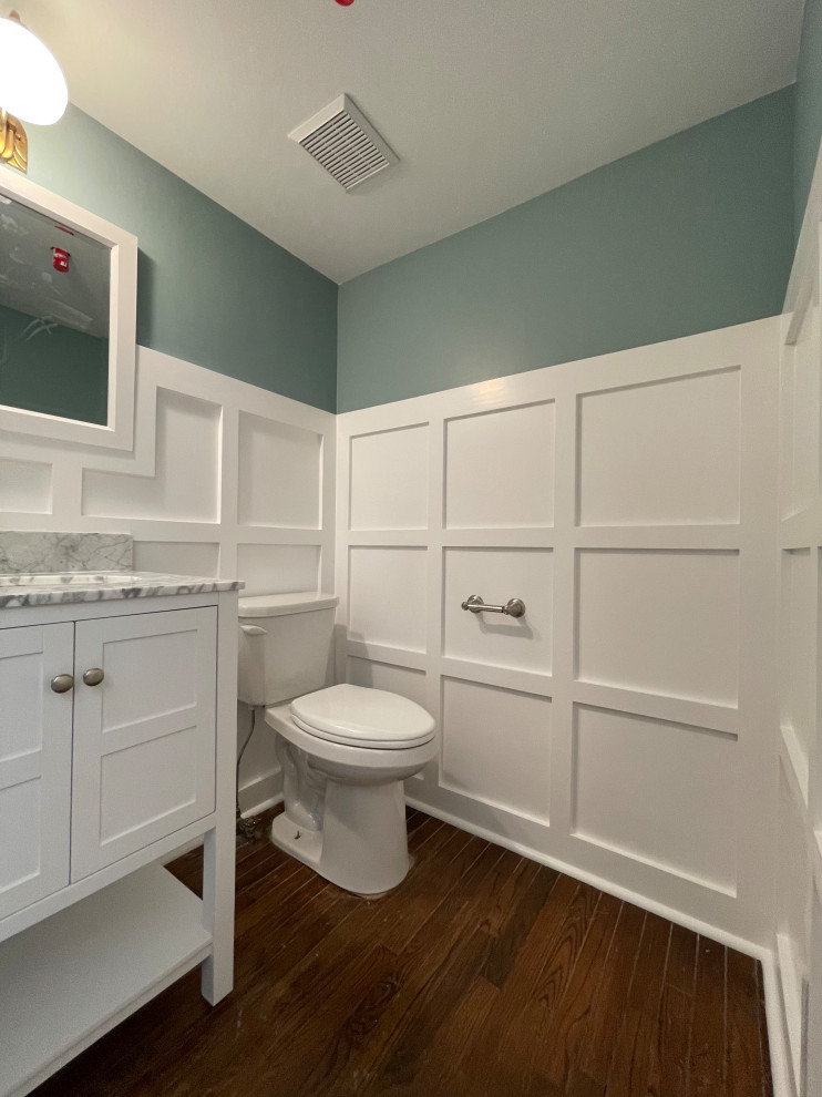 This is an example of a small arts and crafts powder room in Philadelphia with flat-panel cabinets, white cabinets, a two-piece toilet, green walls, dark hardwood floors, an integrated sink, engineered quartz benchtops, multi-coloured benchtops, a freestanding vanity and panelled walls.