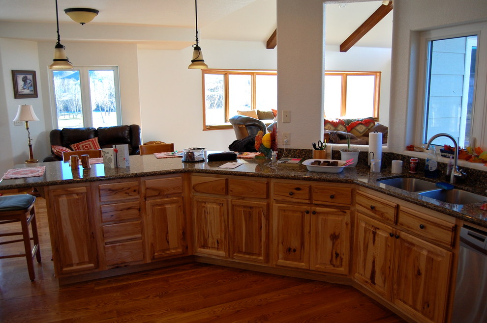 Photo of a traditional u-shaped kitchen in Other with a double-bowl sink, raised-panel cabinets, medium wood cabinets, granite benchtops, dark hardwood floors, a peninsula, brown floor and brown benchtop.