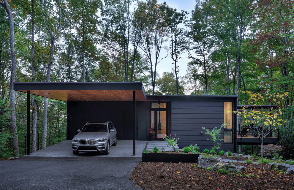 На фото: двухэтажный, черный частный загородный дом в современном стиле с плоской крышей и отделкой планкеном с