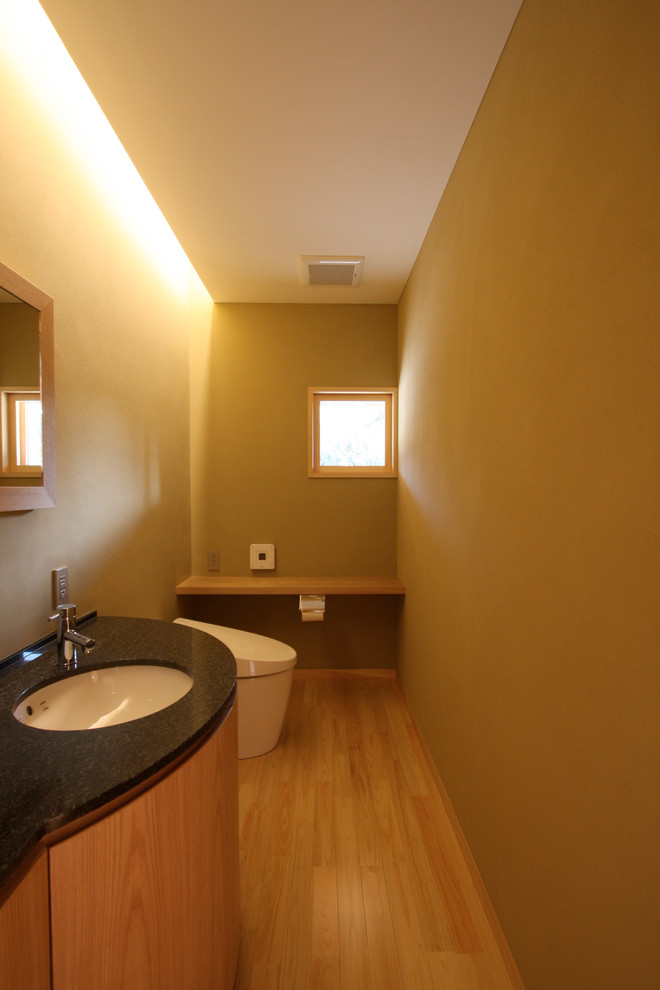 Design ideas for a small asian powder room in Fukuoka with beaded inset cabinets, light wood cabinets, a one-piece toilet, beige walls, light hardwood floors, an undermount sink, granite benchtops, beige floor and black benchtops.