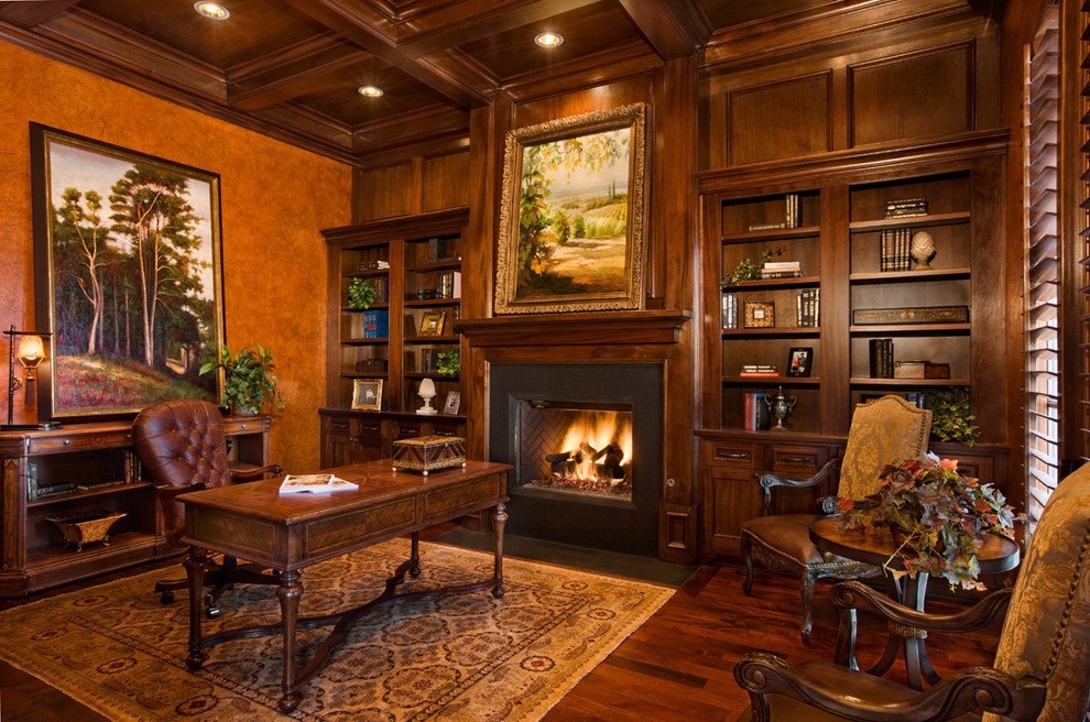 Photo of a traditional study room in Austin with brown walls, dark hardwood floors, a standard fireplace, a metal fireplace surround, a freestanding desk and brown floor.