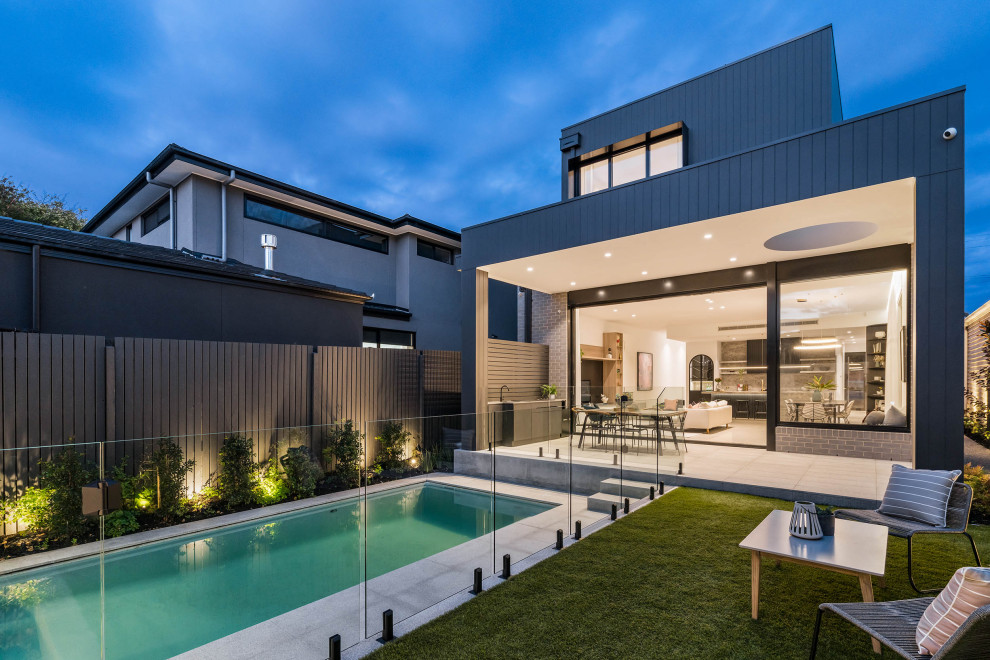 This is an example of a large contemporary two-storey black house exterior in Melbourne with wood siding, a flat roof, a metal roof and board and batten siding.