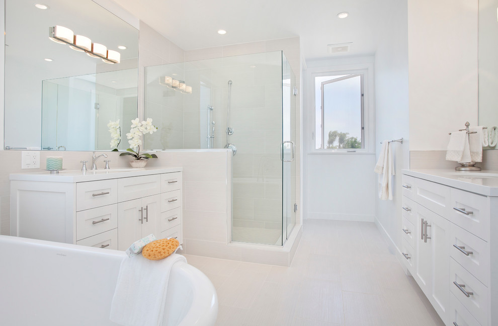 Mid-sized beach style master bathroom in Los Angeles with recessed-panel cabinets, white cabinets, a freestanding tub, white tile, ceramic tile, white walls, ceramic floors, a drop-in sink, a hinged shower door, a corner shower, engineered quartz benchtops, grey floor, white benchtops, a double vanity and a built-in vanity.