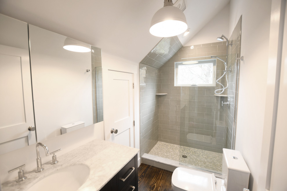 Photo of a mid-sized country kids bathroom in New York with flat-panel cabinets, dark wood cabinets, an alcove shower, a two-piece toilet, gray tile, ceramic tile, white walls, dark hardwood floors, a drop-in sink, engineered quartz benchtops, brown floor, an open shower and grey benchtops.
